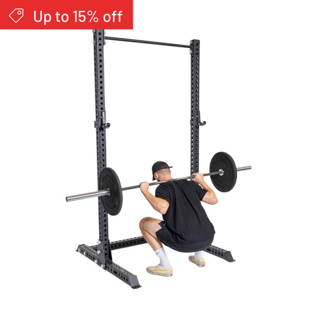 A person in a black shirt and shorts uses the Bells of Steel Manticore Squat Stand Builder (3" x 3", 1" Holes) for barbell squats. A red banner at the top left says "Up to 15% off.