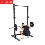 A person in a black shirt and cap performs a barbell squat on the Bells of Steel Manticore Squat Stand Builder (3" x 3", 1" Holes). A red "10% off" banner appears top left, over a plain white background ideal for home gyms.