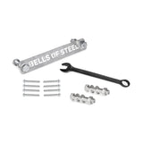 Manticore Hardware by Bells of Steel—including a metal bar, black wrench, bolts, nuts, screws, and concrete anchor bolts—is neatly arranged on a white surface, ready for power rack assembly.