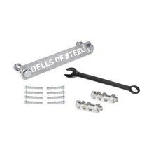 Manticore Hardware by Bells of Steel—including a metal bar, black wrench, bolts, nuts, screws, and concrete anchor bolts—is neatly arranged on a white surface, ready for power rack assembly.