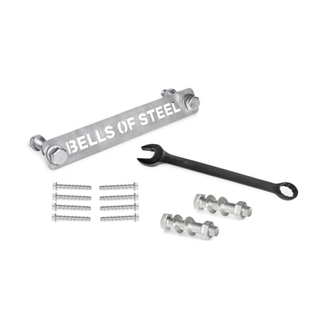 Manticore Hardware by Bells of Steel—including a metal bar, black wrench, bolts, nuts, screws, and concrete anchor bolts—is neatly arranged on a white surface, ready for power rack assembly.