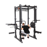 Inside a Bells of Steel Manticore Flat Foot Power Rack, someone in a black shirt and gray shorts performs a squat with a barbell. The rack has a sturdy 1,000-pound capacity and includes various attachments, like weight storage pegs.