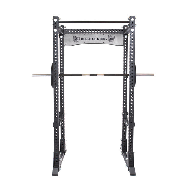 The Bells of Steel Manticore Flat Foot Power Rack - Prebuilt, features a sleek black and metallic finish. It offers an open ecosystem with multiple 1" adjustment holes, a pull-up bar, and can handle up to 1,000 pounds. The brand logo is displayed on the top support bar.