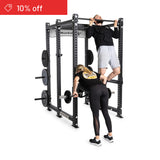 A man does a pull-up on the Bells of Steel Manticore Six Post Power Rack Builder (3" x 3", 1" Holes) while a woman lifts a barbell. A red 10% off tag appears above four stored weight plates—ideal for any home gym setup.