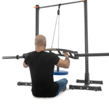 A person sits on the floor using a seated lat pulldown machine with a Bells of Steel Omni Bar and landmine attachment, gripping the knurling on the barbell with both hands, facing away from the viewer.