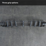 The Bells of Steel Arch Nemesis Swiss Bar, featuring three grip options, rests on a gray tiled floor. "Three grip options" appears in white text—making it an ideal specialty barbell for any bench builder’s collection.