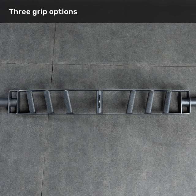 The Bells of Steel Arch Nemesis Swiss Bar, featuring three grip options, rests on a gray tiled floor. "Three grip options" appears in white text—making it an ideal specialty barbell for any bench builder’s collection.