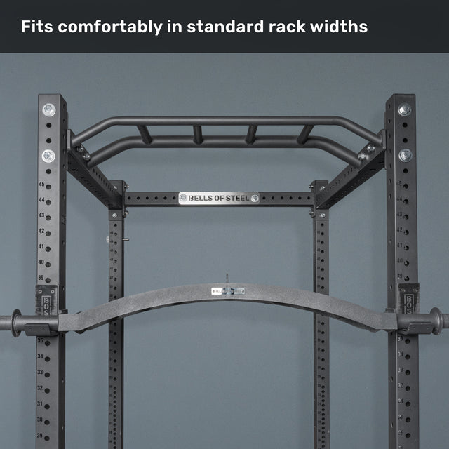 A pull-up bar attachment mounted on a black Bells of Steel power rack against a gray wall, with "Fits comfortably in standard rack widths" at the top—ideal with cable attachments or specialty bars like the Arch Nemesis Swiss Bar.
