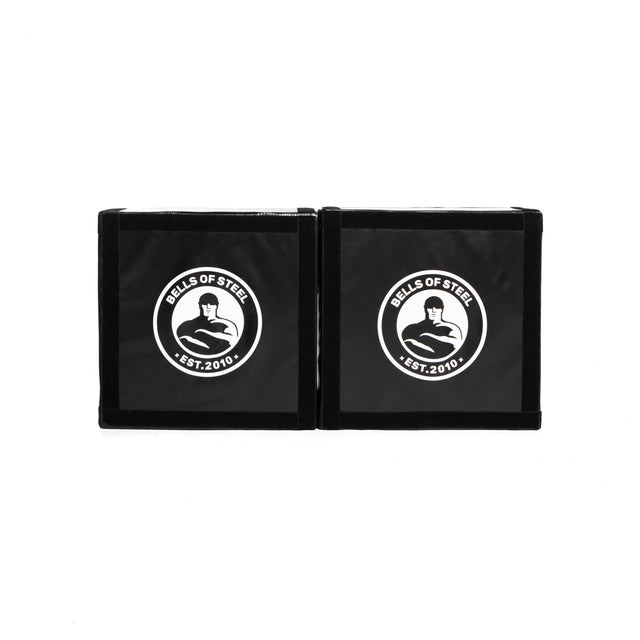 The Bells of Steel Deadlift Platform Drop Pad Pair features two black square pads with a white logo, flexed arm, and "EST. 2010" on each pad. Placed side by side, they reduce noise and absorb impact.