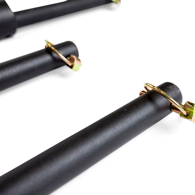 Close-up of black cylindrical metal rods with golden clips attached at the ends. The image shows three rods arranged diagonally, resembling the Bells of Steel Pin Pipe Safeties used in a power rack, highlighting texture and fastening mechanisms for optimal training safety.