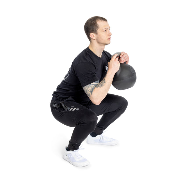 A person in black demonstrates perfect form with a Bells of Steel Plastic Bottom Adjustable Kettlebell during a squat, holding it close to their chest. Against a white background and wearing white athletic shoes, they show seamless transitions in weight increments.