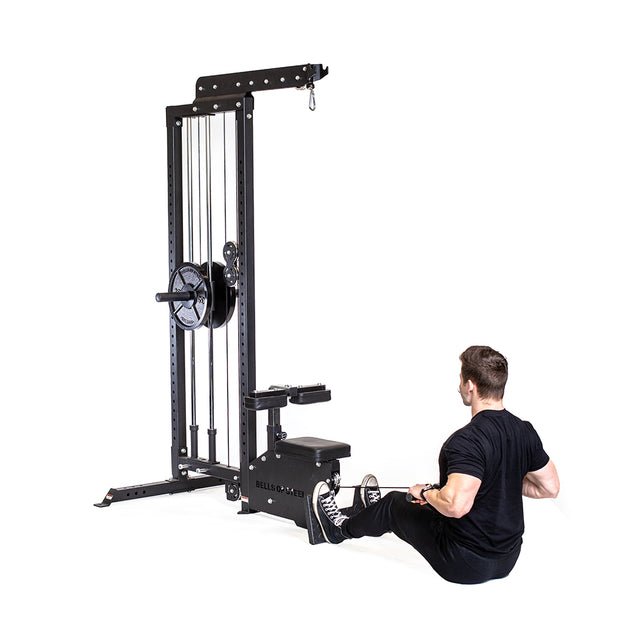 A person in workout gear uses the Bells of Steel Lat Pulldown Low Row Machine, ideal for a home gym. This black machine, fitted with weights and cables, enables a classic rowing motion as they pull the cable towards their body.