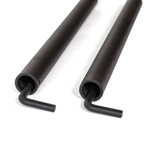 Two black metal rods with cylindrical bodies and hooked ends, resembling Bells of Steel's Pin Pipe Safeties, are positioned parallel to each other on a white surface.