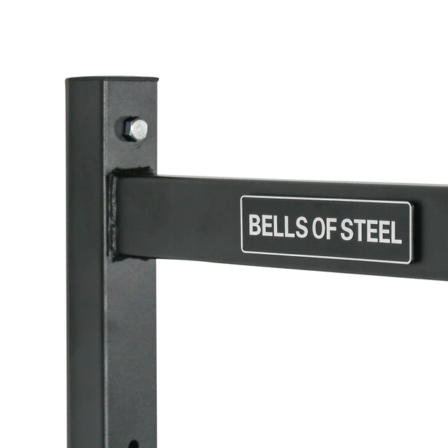 Close-up of a metal rack labeled "Bells of Steel," showing a corner section with a vertical post and horizontal bar connected by a bolt. The sturdy design makes this "Adjustable Wall Or Ceiling Mounted Pull Up Bar" ideal for gym use and kipping exercises.