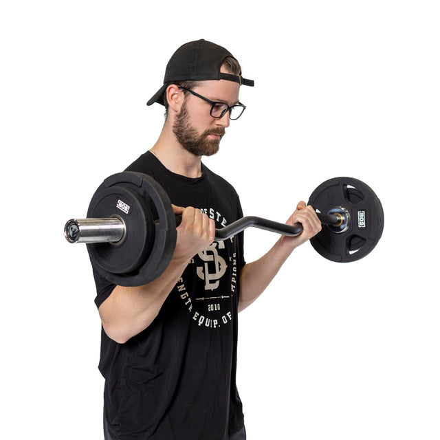 A bearded man in a backward black cap, black glasses, and a black T-shirt performs bicep curls with a barbell using Bells of Steel's Rubber Coated Iron Weight Plates, standing against a white background.