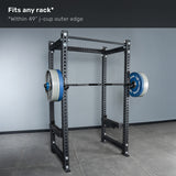 A Bells of Steel Short Rackable Barbell rests on j-cups of a power rack. Text above states, "Fits any home gym rack* *Within 49” j-cup outer edge." The rack is positioned on a tiled floor against a plain gray wall.