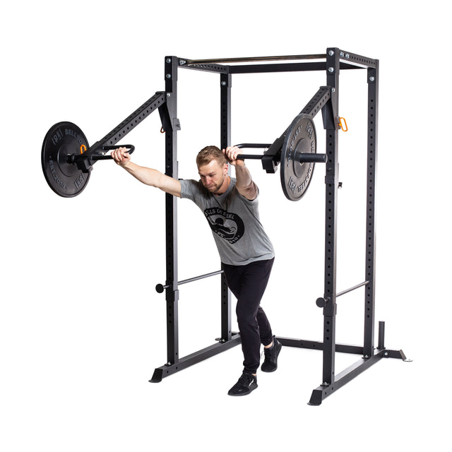 A man in athletic wear performs a chest press with a plate-loaded lever arm on the Bells of Steel Residential Power Rack (2.3" x 2.3", ⅝" holes), leaning forward and pushing the handles away from his chest—perfect for home gyms.