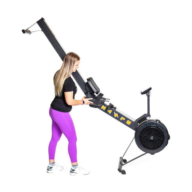 A person in a black shirt and purple leggings adjusts the Blitz Air Rower by Bells of Steel, ideal for low-impact cardio, against a white background.