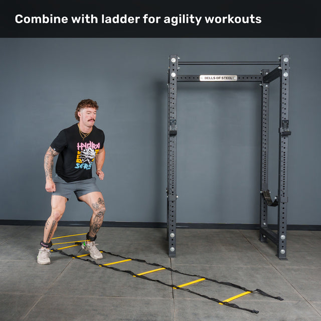 A person performs agility ladder drills on a gym floor near a squat rack, using Bells of Steel USA Human Trainer - Leg Cords to intensify the workout. Text at the top reads, “Combine with ladder for agility workouts.”.