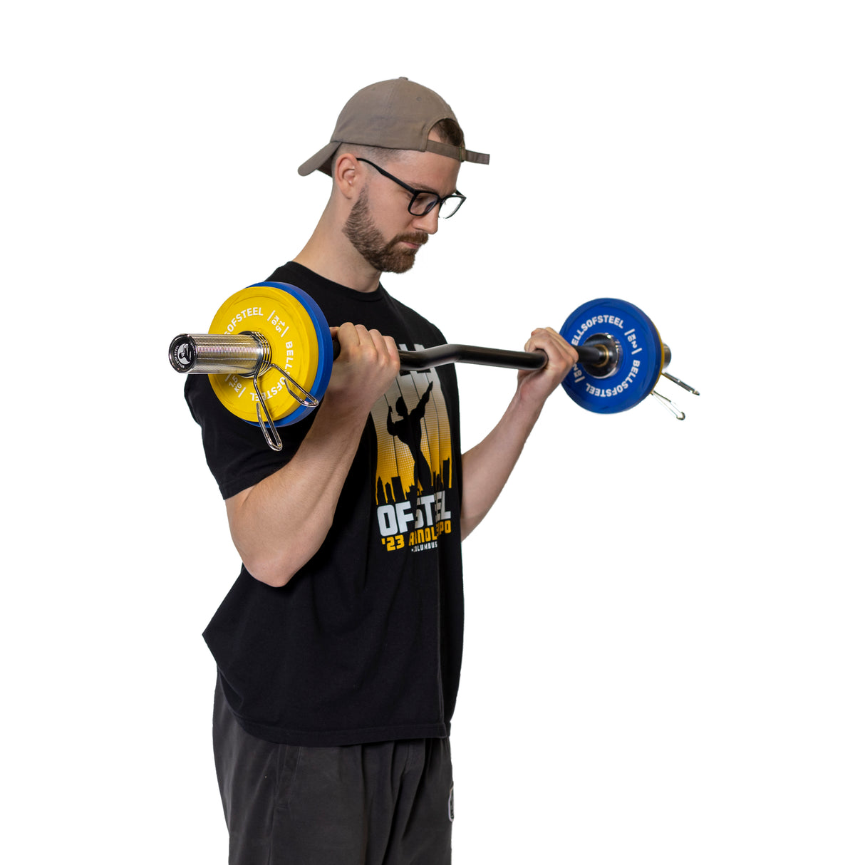 A man wearing a black T-shirt, gray pants, a cap, and glasses lifts a barbell with blue and yellow weight plates secured by Bells of Steel Spring Collars on polished chrome Olympic sleeves against a plain white background.