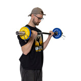 A man in a backward cap, glasses, and black T-shirt performs a bicep curl with a barbell featuring yellow and blue plates secured by Bells of Steel Spring Collars, with a white background.