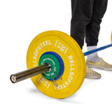A person wearing checkered slip-ons and black pants stands beside a barbell loaded with large yellow and green Bells of Steel plates, secured firmly using Bells of Steel Spring Collars.