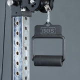 Close-up of a metallic gym cable machine with a Fat Bar - Single D Handle by Bells of Steel hanging from a hook. This handle boosts grip strength, and the vertical post has numbered holes for adjustable height settings.