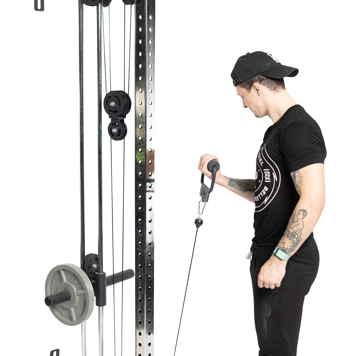 A person wearing a black shirt and cap uses the Bells of Steel Fat Bar - Single D Handle on a weight machine. Standing beside the metal frame, they focus intensely on their workout, enhancing grip strength.