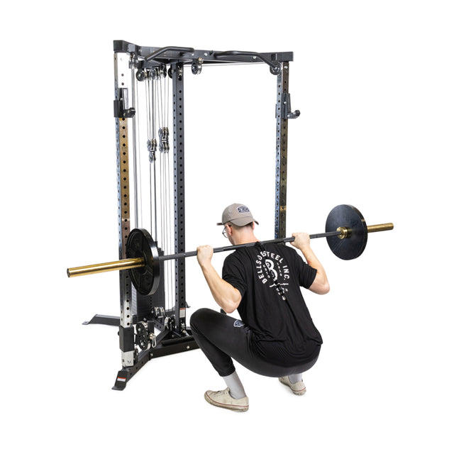 A person in a black t-shirt, black pants, white shoes, and a gray cap squats with a barbell on their shoulders in front of the Bells of Steel All-in-One Trainer.