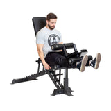 Wearing a gray t-shirt and black pants, a man uses the Bells of Steel bench attachments for leg extensions. He sits on the adjustable bench with legs extended and hands gripping the handles, benefiting from multiple positions designed for optimal comfort.