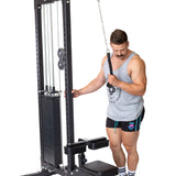A man in a gray tank top and black shorts stands next to a cable machine, holding the Bells of Steel Tricep Pulldown Rope – Single in one hand and preparing to exercise, set against a plain white background.