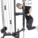 A man in a cap and glasses works out on the Bells of Steel All-in-One Trainer, utilizing weight stacks and pulleys. He's dressed in a black shirt, dark gray sweatpants, and white socks for an efficient exercise session.