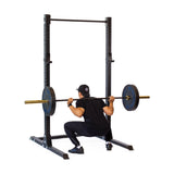 A person using the Bells of Steel Hydra Squat Stand - Prebuilt (3" x 3", ⅝" Holes) performs a squat with a barbell on their shoulders. Wearing black athletic clothing and a cap, they enhance their home gym setup. The barbell is loaded with weight plates on both ends.