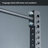 Close-up of the Bells of Steel Manticore Squat Stand Builder (3" x 3", 1" holes) in black metal, featuring laser-cut numbered holes, sturdy bolts, and a horizontal bar. Text at the top reads, "11 gauge steel with laser-cut numbers and 3x3 uprights." Perfect for any home gym setup.