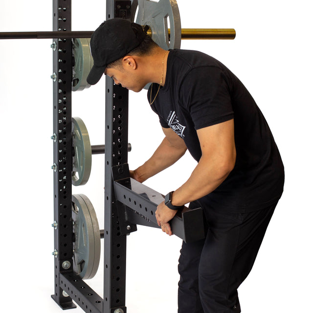 A person in black attire adjusts the Bells of Steel Spotter Arms Rack Attachment, with UHMW lining, to organize weight plates for efficient barbell supersets.