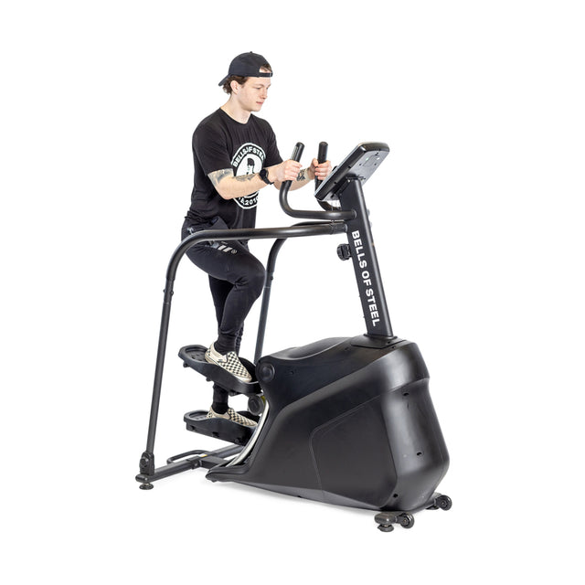A person in black clothes and a backwards cap uses the Bells of Steel Blitz Stepper for low impact cardio against a plain white background.
