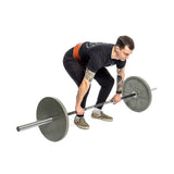 A tattooed individual in black attire and checkered shoes is bending forward to lift a barbell with large weights, gripping the bar while wearing a Bells of Steel USA 10mm Leather Weightlifting Belt for added support.