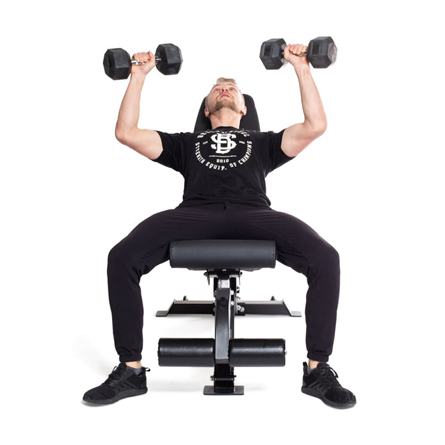 A person in a black t-shirt, pants, and shoes is seated on a black bench using Bells of Steel Straight Handle Rubber Hex Dumbbell Sets for an incline bench press. The chrome-plated handles stand out against the white background.