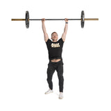 A man in a black "Balls of Steel" shirt and black pants lifts a barbell featuring Bells of Steel Technique Plates - 5 Lbs (Pair) with a virgin rubber coating. He stands determinedly against a white background, showcasing his strength.