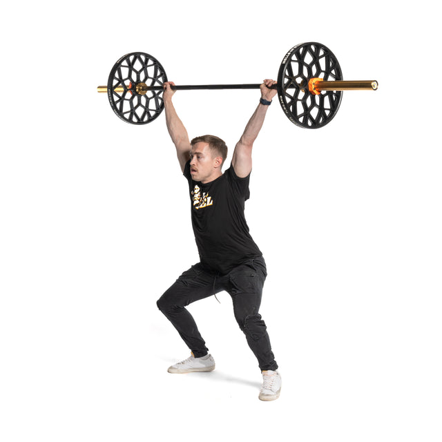 A person in athletic wear performs an overhead barbell lift with Bells of Steel Technique Plates - 5 Lbs, featuring a virgin rubber coating. The weight plates resemble wheels, and the person stands with bent knees, holding the barbell overhead against a plain white background.