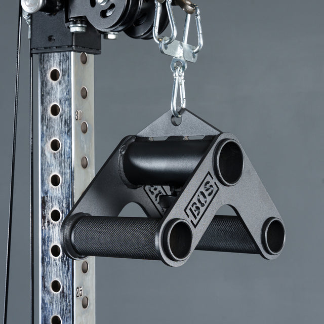 A close-up of the Bells of Steel Fat Bar - T-Bar Row Cable Attachment, featuring a black triangular metal design for enhanced grip strength, hangs from a carabiner on a cable machine against a plain gray background.