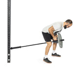 A bearded man wearing a white shirt and black shorts uses the Bells of Steel Fat Bar - T-Bar Row Cable Attachment to perform a bent-over row exercise, showcasing impressive grip strength by gripping the bar with both hands in the gym.