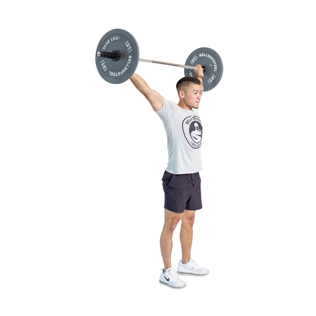 A man wearing a t-shirt and shorts expertly lifts the Bells of Steel Aluminum Technique Barbell against a white backdrop, showcasing his strength and focus.