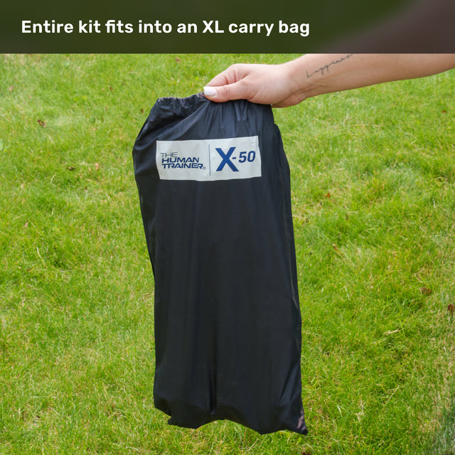 A hand holds a black drawstring bag labeled “Bells of Steel USA” outdoors on green grass. Text above reads, “Entire Agility Ladder and Leg Cord Bundle fits into an XL carry bag.”.