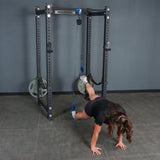 Using the Rotational Pulley from Bells of Steel USA, a person performs an intense bodyweight workout by suspending their feet in straps attached to a squat rack and balancing on their hands on the gym floor.