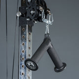 Close-up of the Bells of Steel Fat Bar - Tricep Pressdown, featuring two black rubber handles attached to a metal pulley system with carabiners, ideal for tricep and grip strength training against a plain grey background.