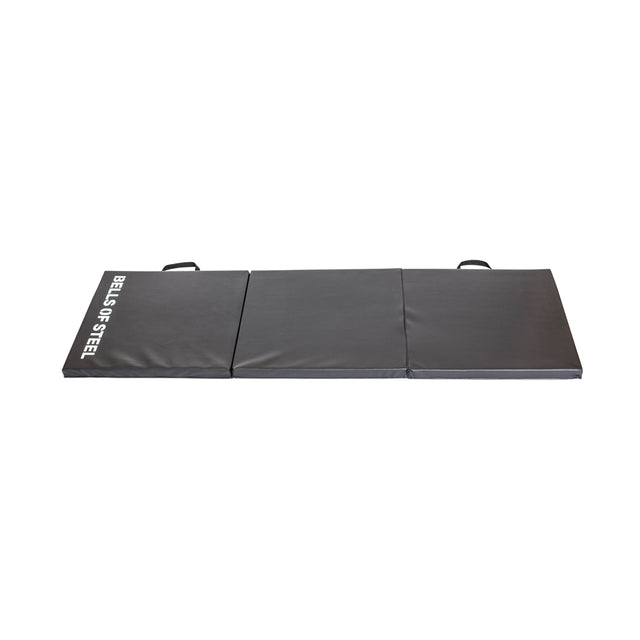 The Wildman Turkish Get Up Kettlebell Bundle by Bells of Steel USA includes a foldable, black exercise mat with three square sections—ideal for your routine. It has handles on two edges, features "BELLS OF STEEL" in white on one section, all against a crisp white background.