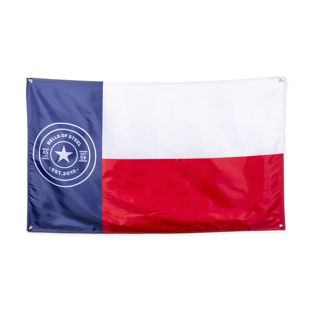 The image displays a Bells of Steel home gym flag inspired by the Texas state flag, with red, white, and blue sections and a central star. A left-side circular logo reads "Bells of Steel Est. 2010" featuring a star—ideal for enhancing your gym decor.