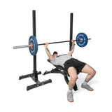 A person in athletic wear performs a bench press on the Bells of Steel Adjustable Utility Bench, lifting a barbell with blue plates inside a black power rack with a 575lb max capacity.