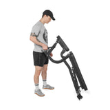 A man in athletic wear and a cap adjusts the Bells of Steel Adjustable Utility Bench (575lb max capacity), standing on a white background.